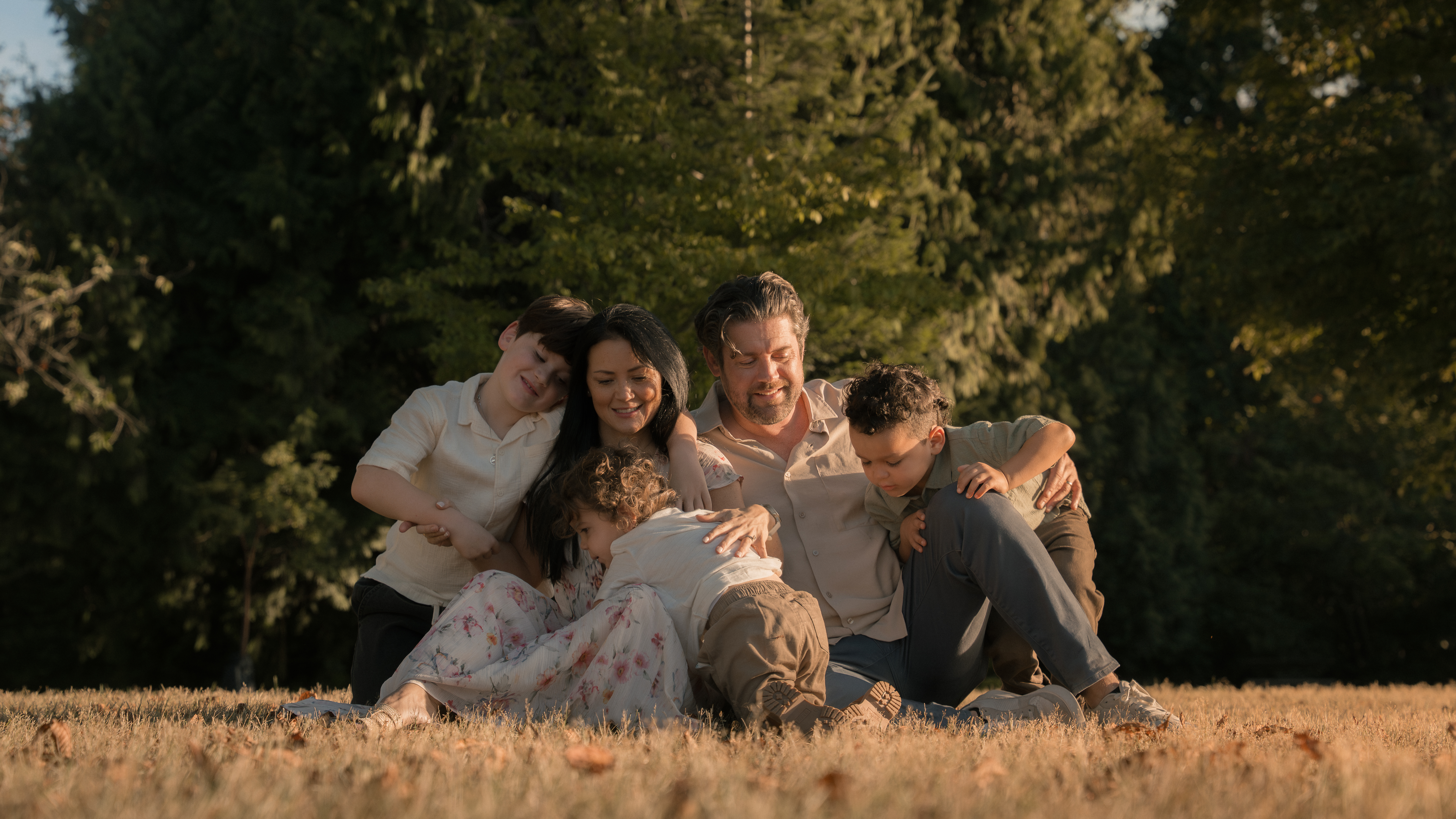 A family leaning closely together while seated in a sunlit field
